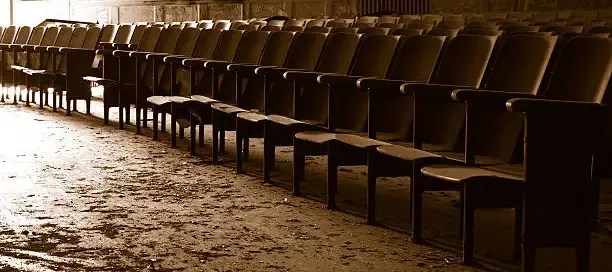 Rows of empty, aged theater seats in warm sepia light, evoking distance and quiet disuse.