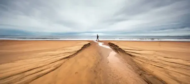 A person walking on a quiet, overcast beach.
