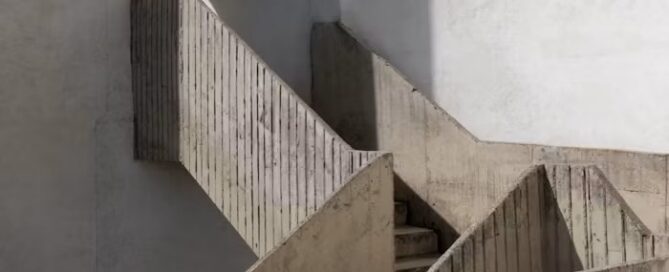 Minimalist concrete staircase turning a corner, with soft light and geometric shadows.