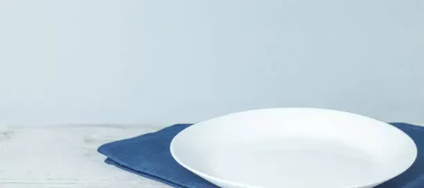 Single white plate on a blue napkin resting on a light, weathered surface.